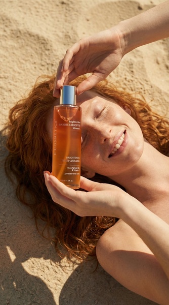 A close-up, high-angle shot of a woman holding a bottle of Brightening Toner while resting on sand, evoking a natural and organic brand feeling.